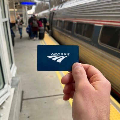 amtrak Hand holding Amtrak card in front of train.